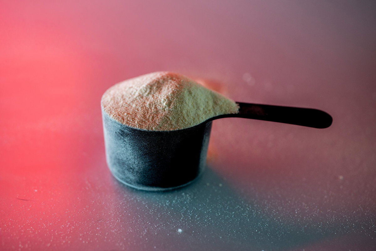 Löffel mit Proteinpulver auf einem rötlich angeleuchteten Hintergrund